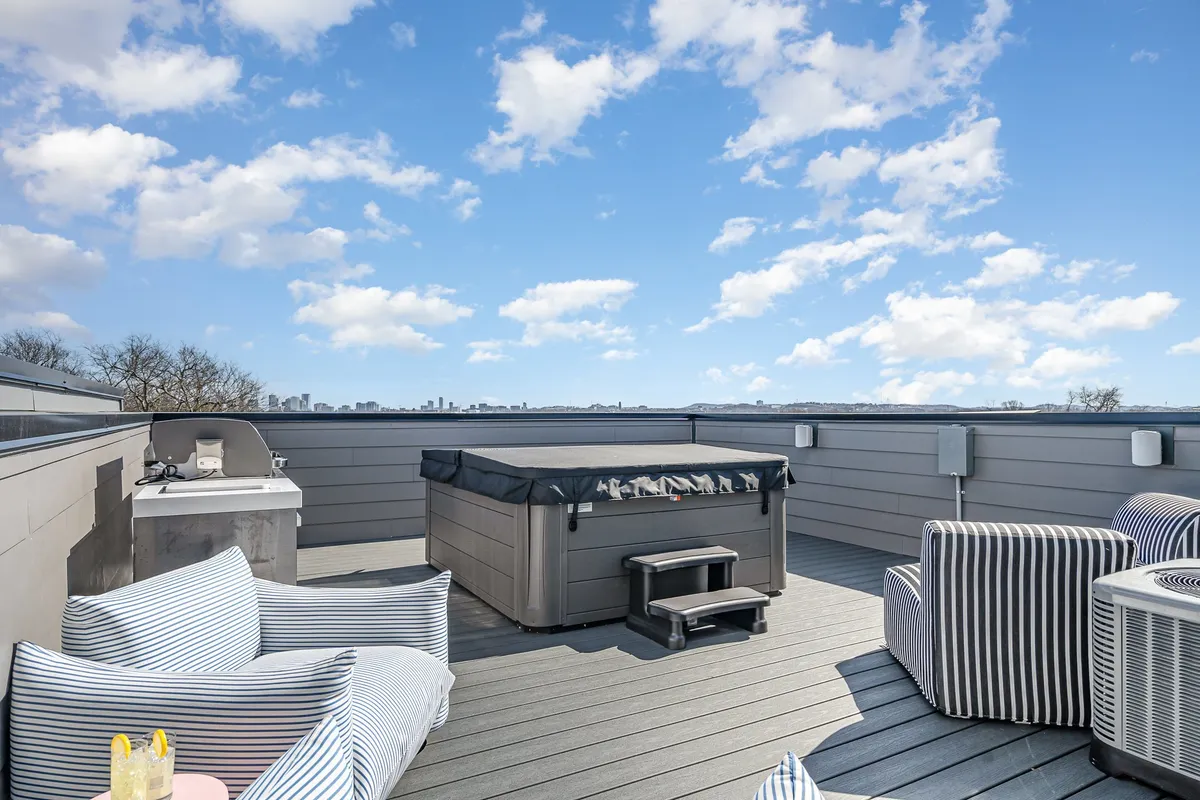 An outdoor rooftop space with a bubbling hot tub, striped lounge chairs, and an outdoor grill. The scene captures a relaxed and casual atmosphere, perfect for stargazing, dining, or enjoying a morning coffee with expansive urban views.