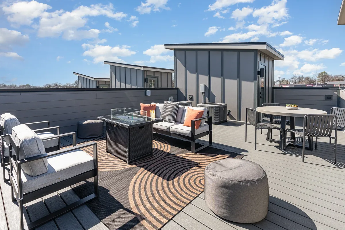 A contemporary rooftop lounge area with a glass table, plush outdoor seating, and a decorative rug, set beneath the open sky. The setting is inviting, ideal for entertaining friends, enjoying sunset views, and intimate fireside conversations.