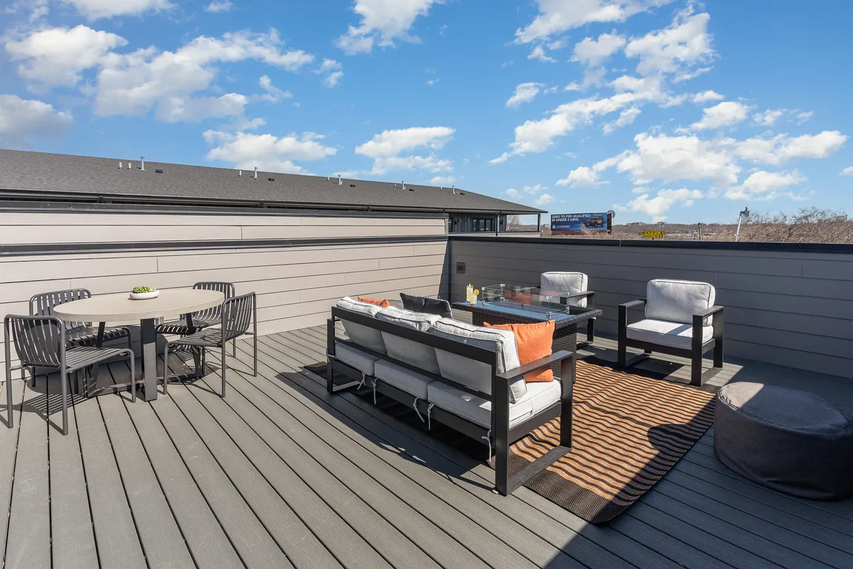 An inviting outdoor seating area featuring a spacious dining table, decorative rug, and comfortable chairs arranged for social gatherings. The scene is bathed in natural light, suggesting a welcoming environment for brunches or evening relaxation with the city as a backdrop.