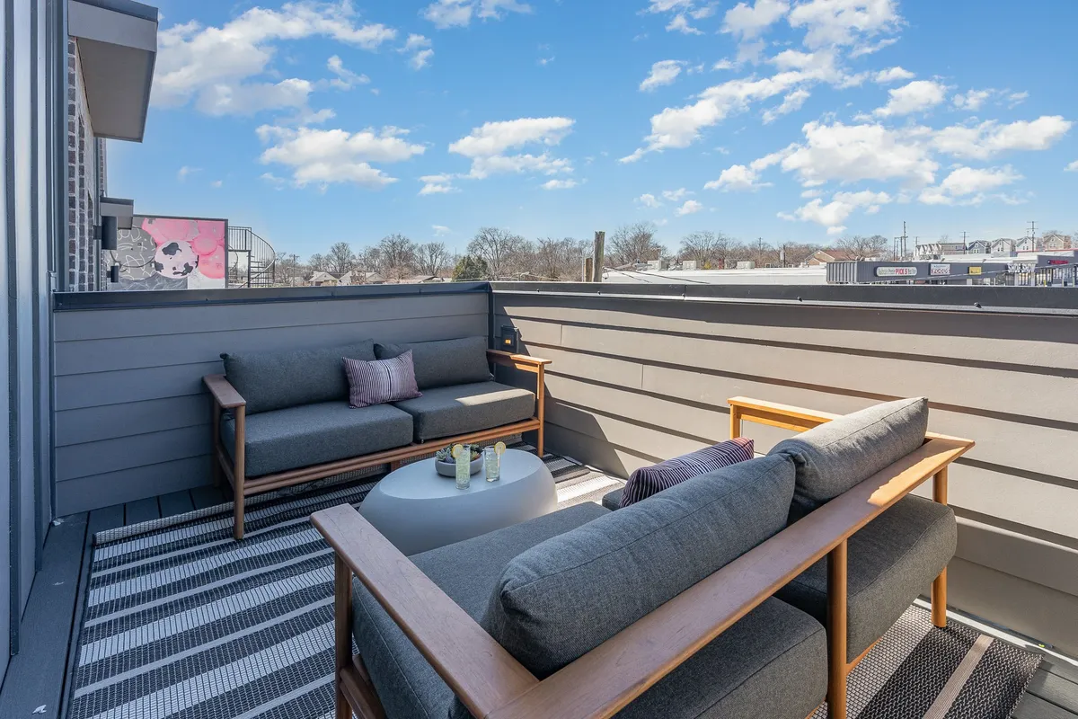 This image captures a modern outdoor seating area with a small circular table, textured outdoor rug, and city skyline views in the background. The setting is ideal for enjoying drinks at sunset or winding down after a day exploring the city.