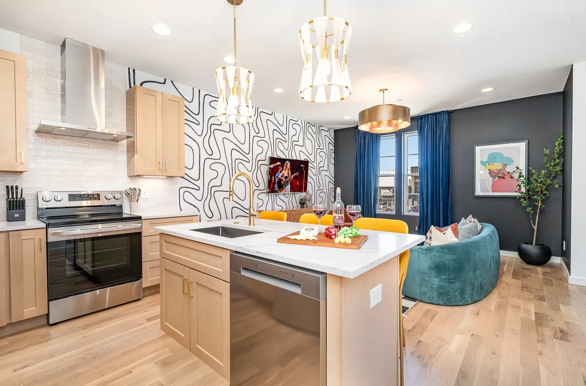 A bright and colorful kitchen interior with a kitchen island, modern appliances, artistic wall design, and a cozy seating area, reflecting a fully equipped and welcoming space.