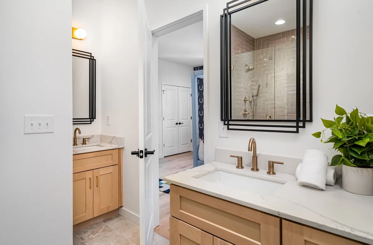 A modern bathroom with dual sinks, mirrors, sleek fixtures, a shower area, and a touch of greenery. The space is bright, serene, and thoughtfully designed for personal grooming or winding down after a busy day.