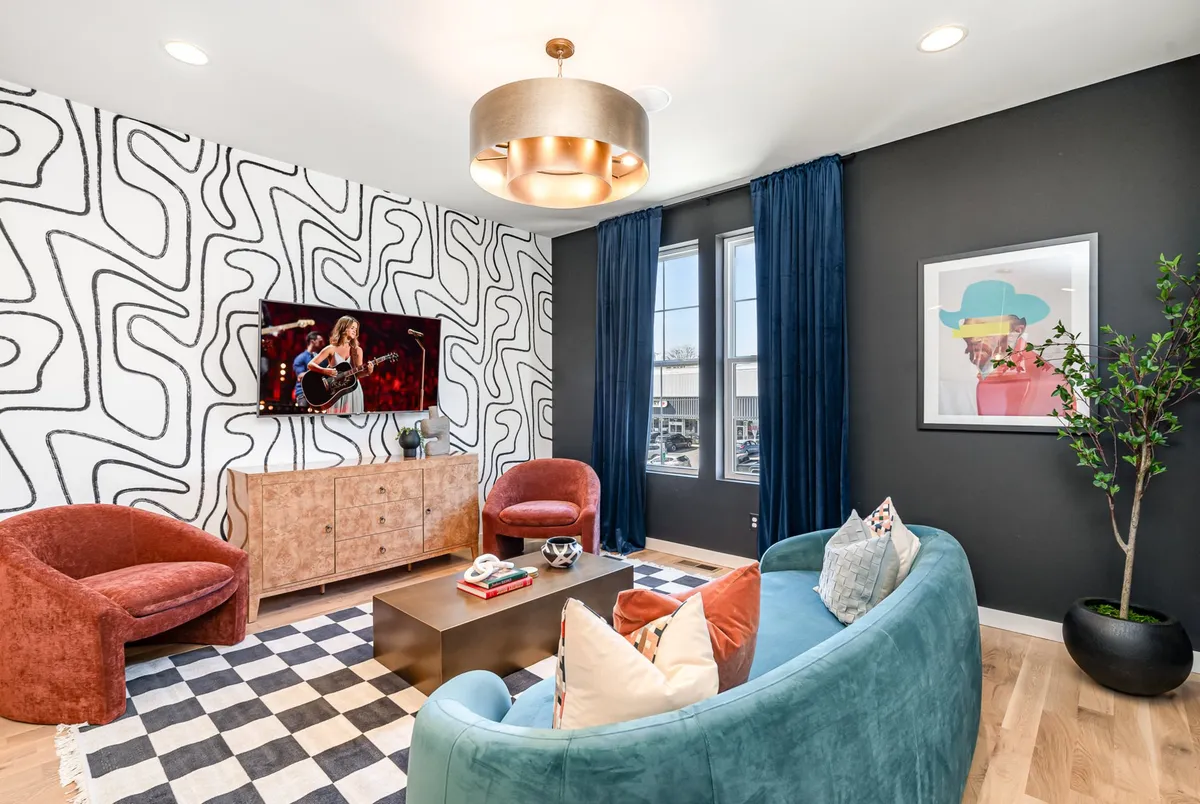 A vibrant living room featuring colorful sofas, unique wallpaper, a large TV display, and decorative art pieces. The design is bold and artsy, creating an inviting space for gatherings, movie nights, and art appreciation.