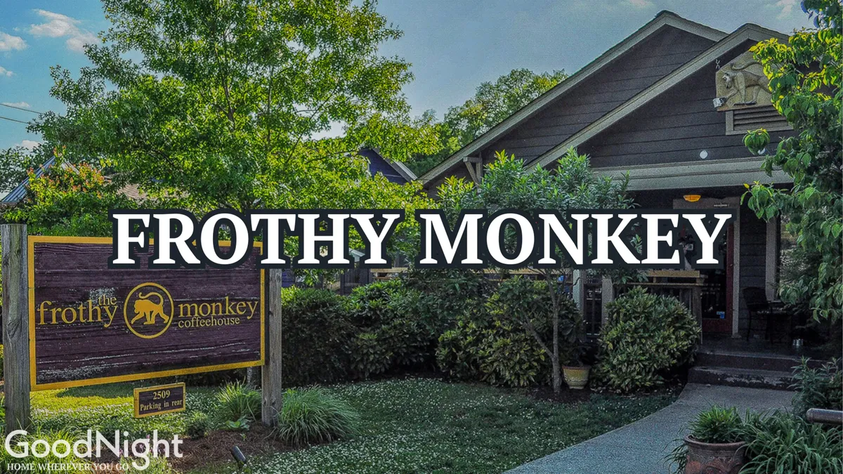 The image features the charming exterior of Frothy Monkey coffeehouse, with its distinctive signage prominently displayed. Lush greenery surrounds the building, creating a welcoming and vibrant outdoor atmosphere. People are seen enjoying coffee and socializing on the patio.