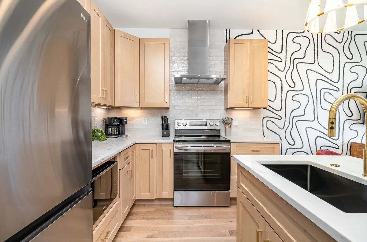 A contemporary kitchen equipped with stainless steel appliances, a marble countertop, unique wall art, and gold accents. The open layout encourages cooking, entertaining, and group gatherings.