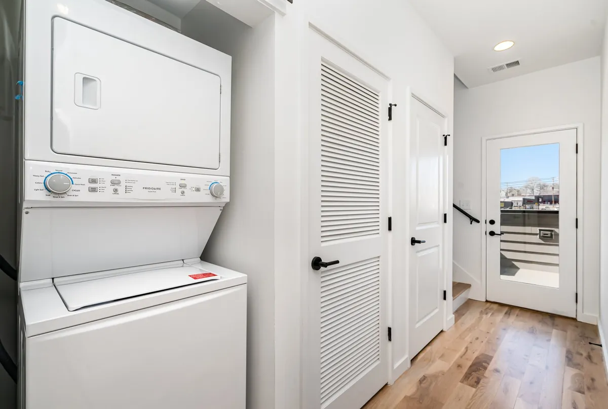 An interior shot highlighting a laundry area equipped with a washer and dryer, a door leading to the outdoor space, and a clean, functional design.