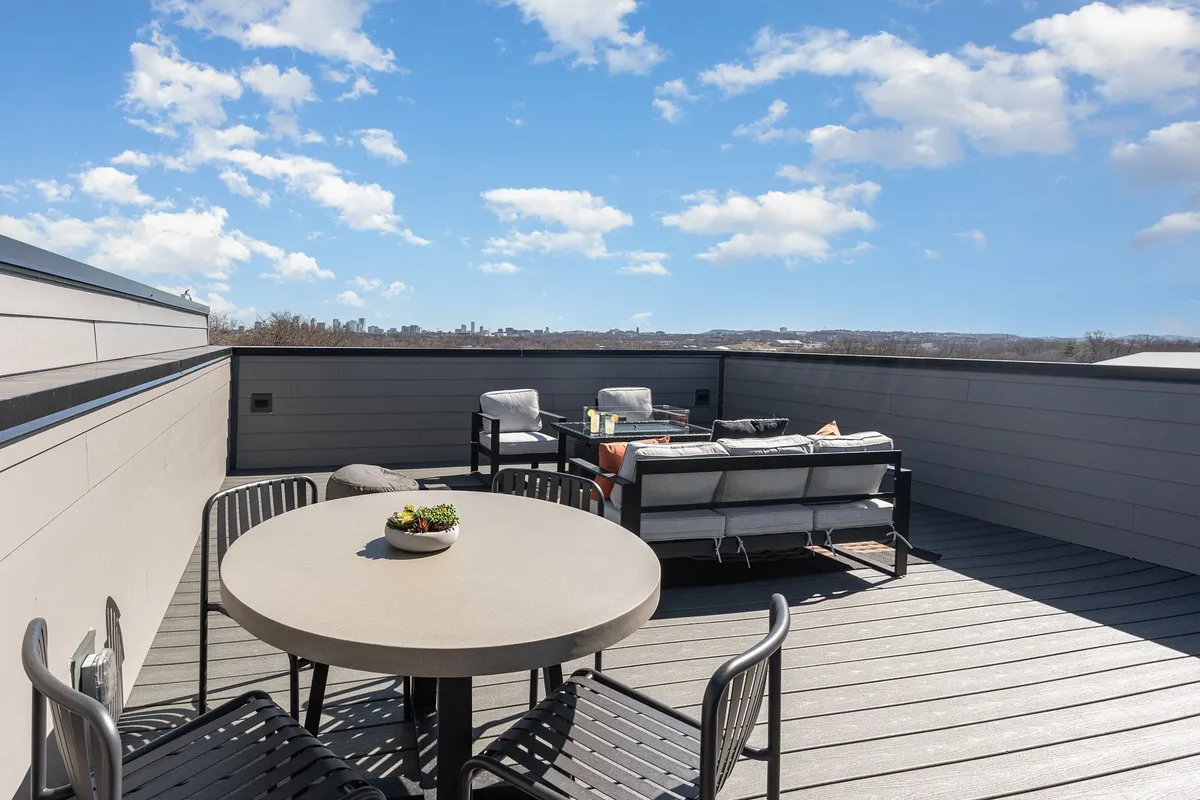 A rooftop outdoor seating area with a dining table, overlooking the sparkling city skyline. The scene captures a tranquil yet sophisticated vibe, ideal for unwinding with friends after an evening downtown.
